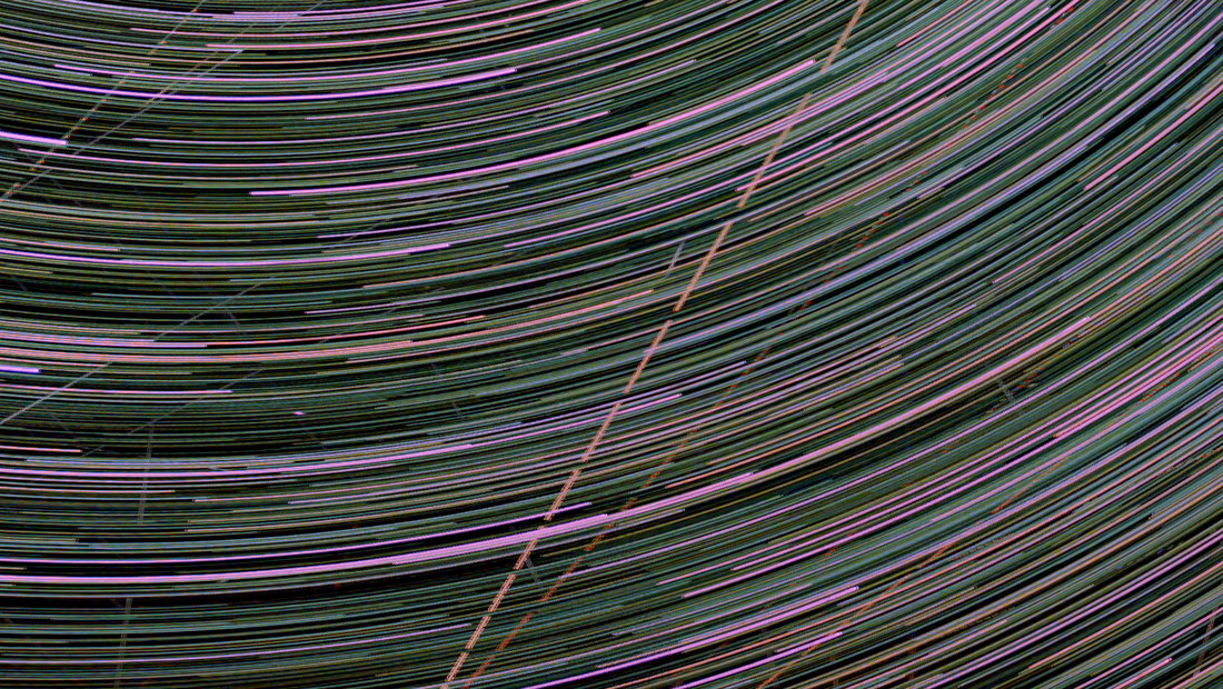A crop of the star-trail stack with a straight track left in: one bright diagonal line cutting corner to corner across the concentric arcs