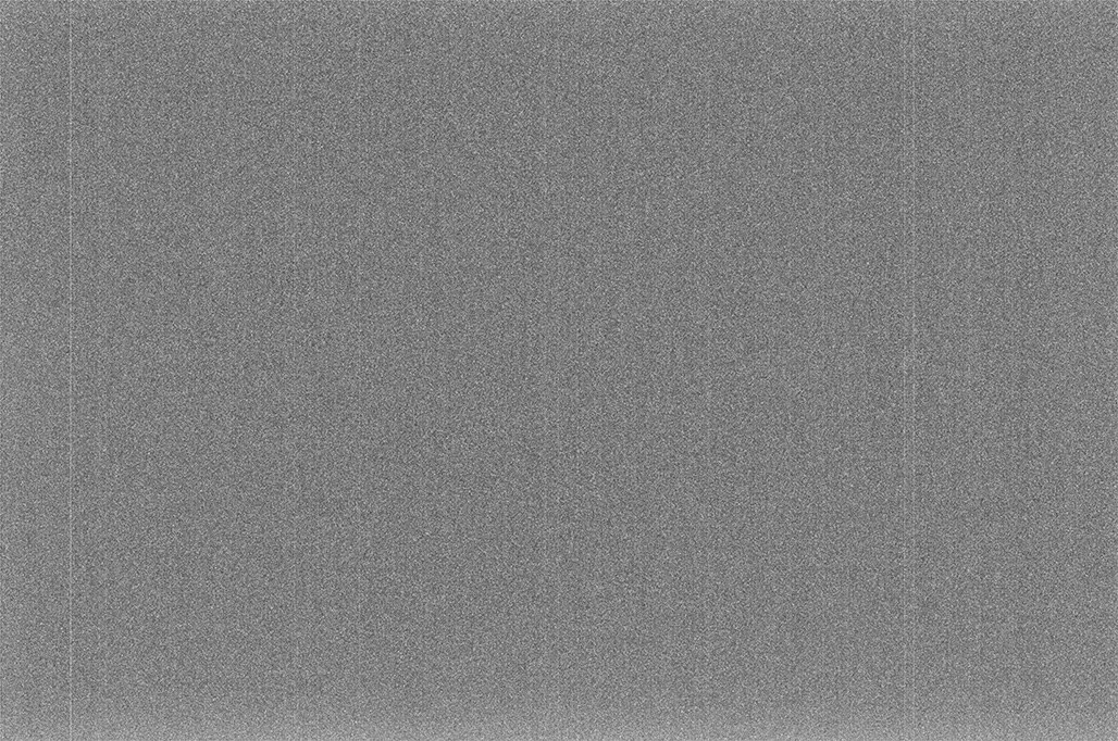A master dark frame from a DSLR, contrast-enhanced: a dark field with a fine speckle of hot pixels and a faint large-scale pattern across it